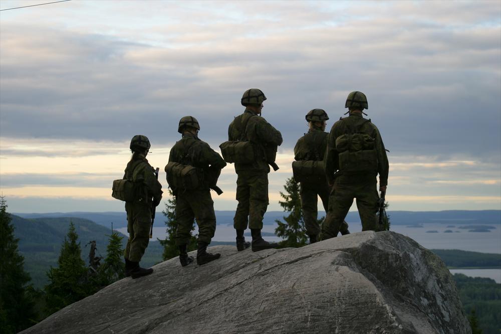 Four conscripts stand on a cliff with a view down to a lake
